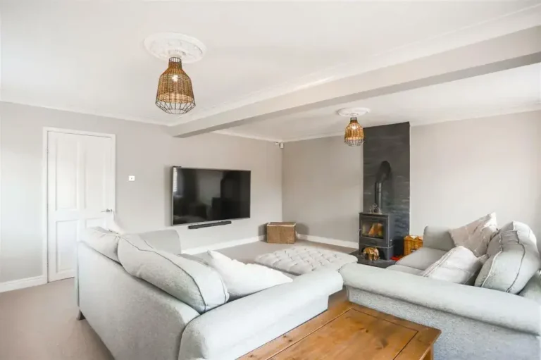 A modern living room with two light gray sofas, a large wall-mounted TV, a wood-burning stove, and two wicker light fixtures. A wooden coffee table sits in the center.